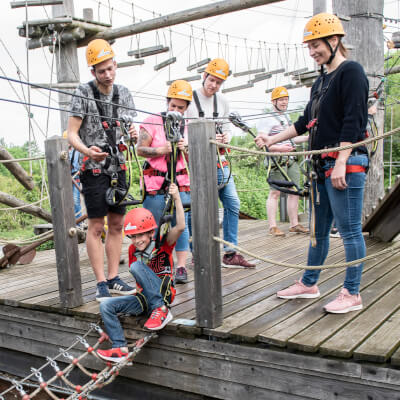 Mehrere Besucher stehen auf einer Plattform und schauen einem Kind beim Klettern zu